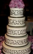 White buttercream iced,  5 tier round wedding cake decorated with black piped scrollwork ribbon.  Fresh Roses as the topper.   (This cake can serve receptions with 250-380 expected guests)